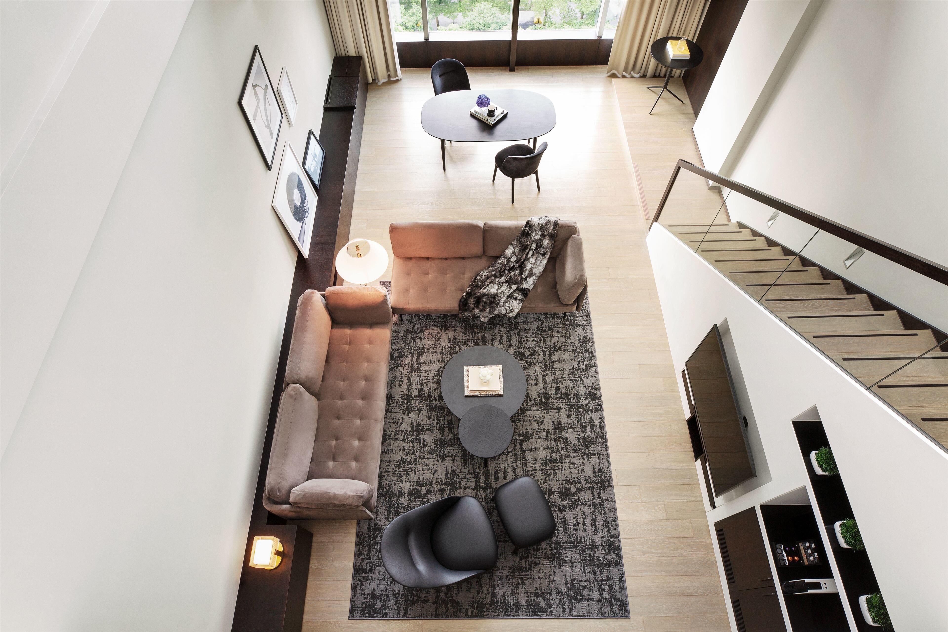 Una sala moderna con sofá, mesa de centro y sillas, un comedor con mesa y sillas, y una escalera que sube a un nivel superior.