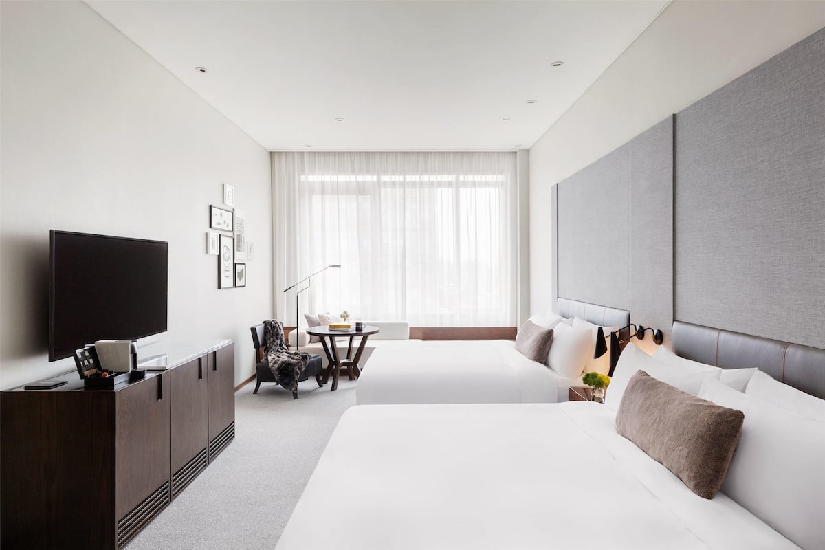 Habitación de hotel moderna con una cama grande, televisor, escritorio y ventana con cortinas traslúcidas.