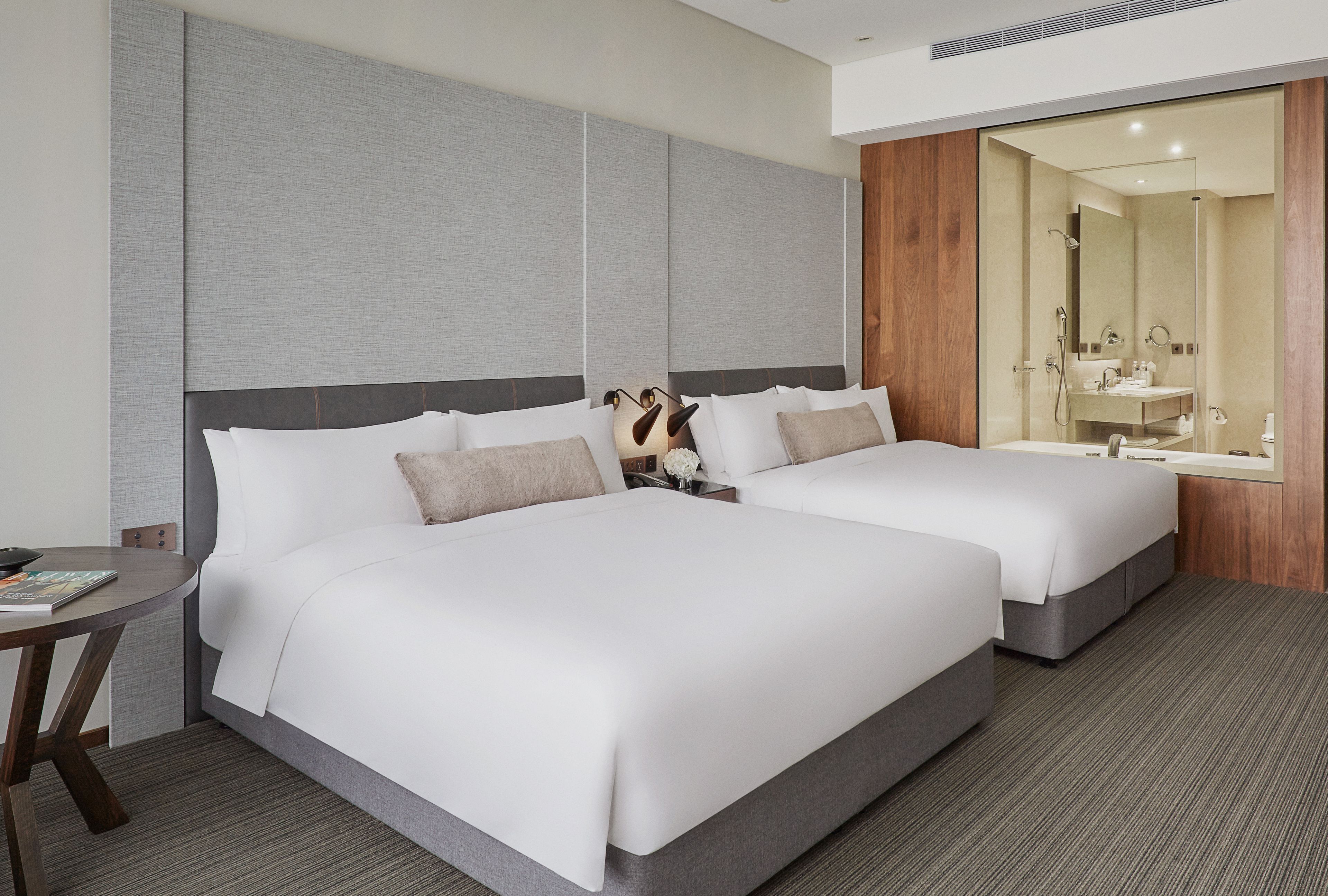 A hotel room with two beds, a small table, and a bathroom with a mirror and sink.