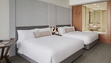 A hotel room with two beds, a small table, and a bathroom with a mirror and sink.