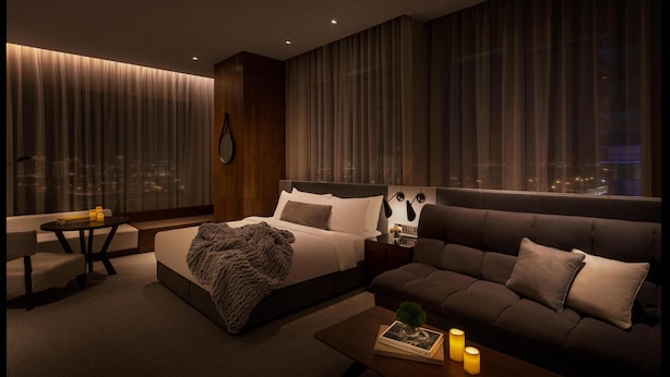 Een moderne hotelkamer met een groot bed, een bank, een kleine tafel en uitzicht op de stad 's nachts.