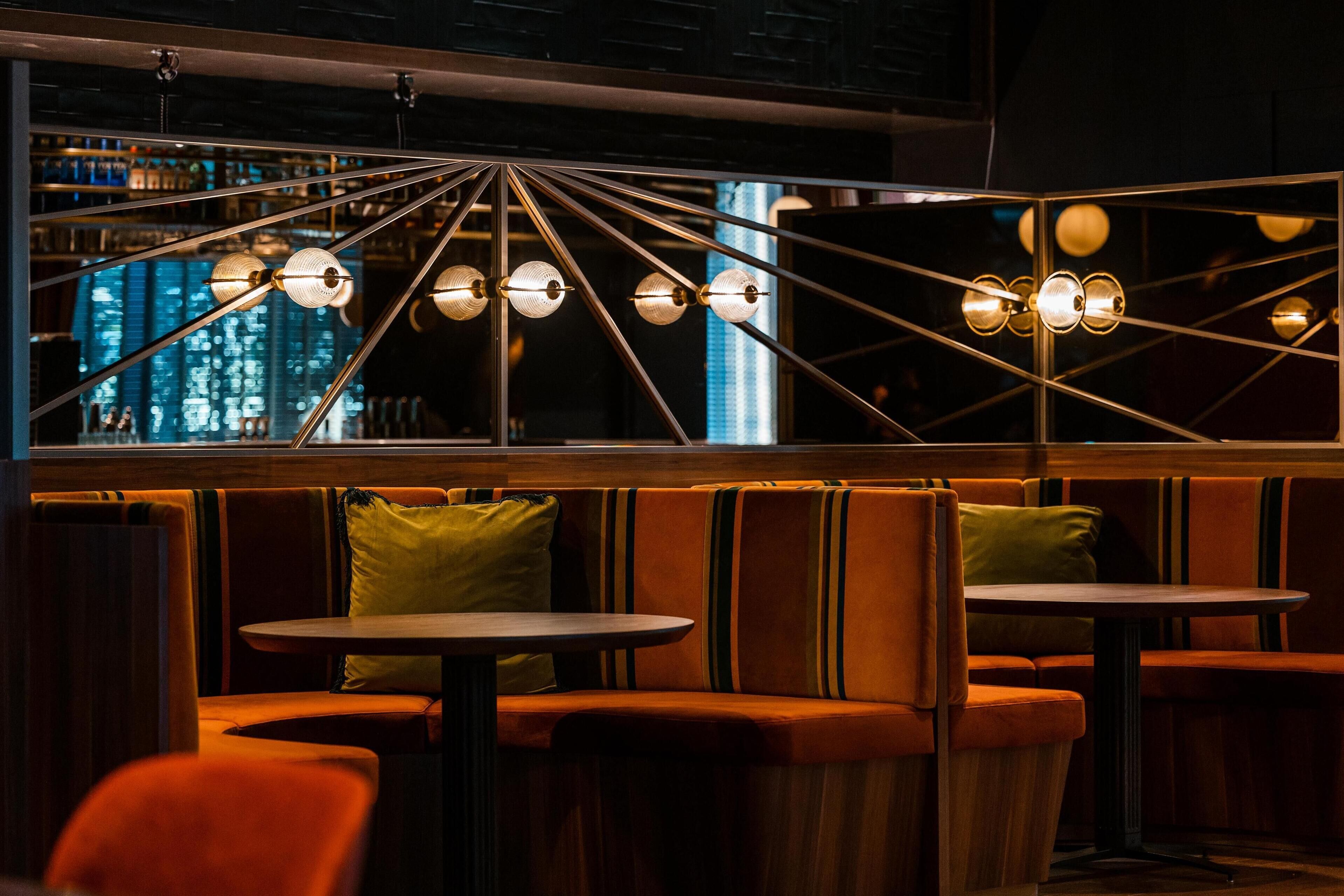 A modern interior with a seating area featuring cushioned booths and round tables, illuminated by a geometric ceiling light fixture.
