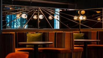 A modern interior with a seating area featuring cushioned booths and round tables, illuminated by a geometric ceiling light fixture.