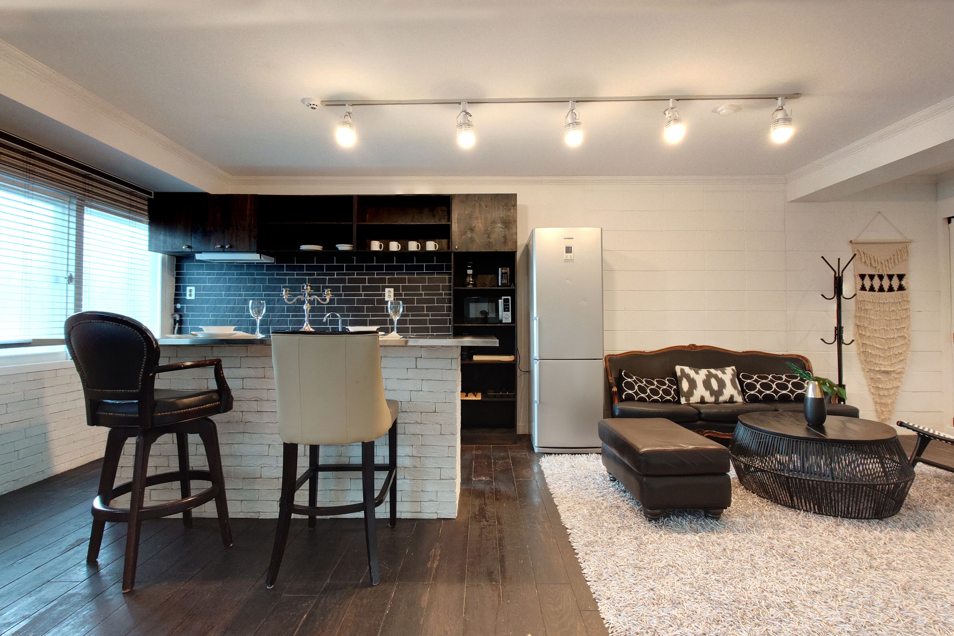A modern kitchen with dark wooden cabinets, a white brick backsplash, and a built-in island with bar stools.