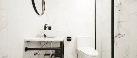 Un baño con inodoro blanco, lavamanos con espejo y zona de ducha.