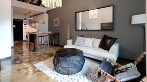 Ein modernes Wohnzimmer mit einem weißen Sofa, einem runden schwarzen Couchtisch und einem Essbereich mit Tisch und Stühlen.