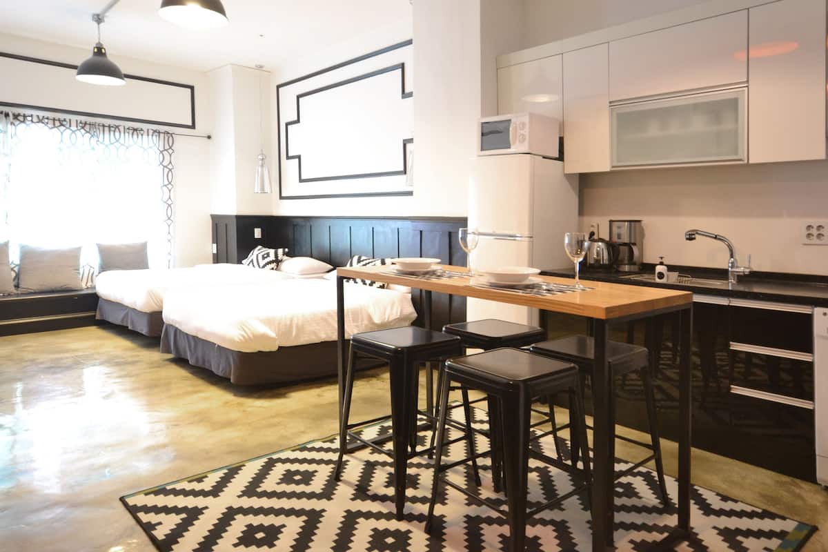 Habitación de hotel compacta con cama, mesa de comedor, taburetes de bar, lavadora y microondas.