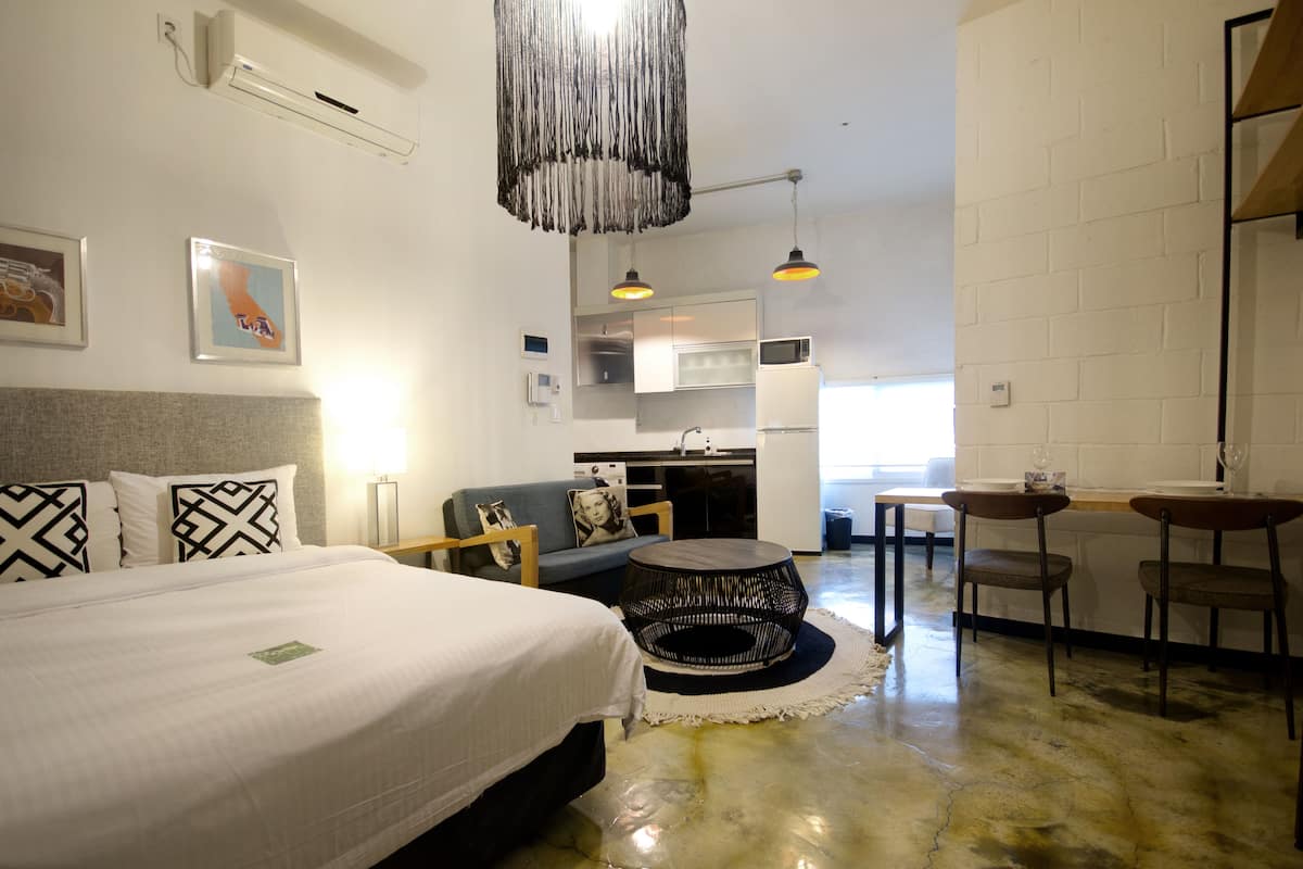 Una habitación de hotel moderna con cama, sofá, zona de comedor y kitchenette.