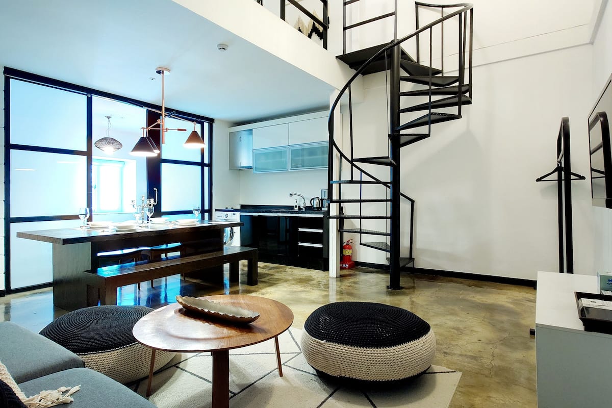Una cocina moderna con una escalera espiral, un comedor con un banco y un ventanal que proporciona luz natural.