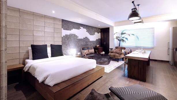Ein modernes Schlafzimmer mit einem großen Bett, einer Sitzecke mit Sofa und Sesseln, einem kleinen Tisch und einer Wandverzierung.