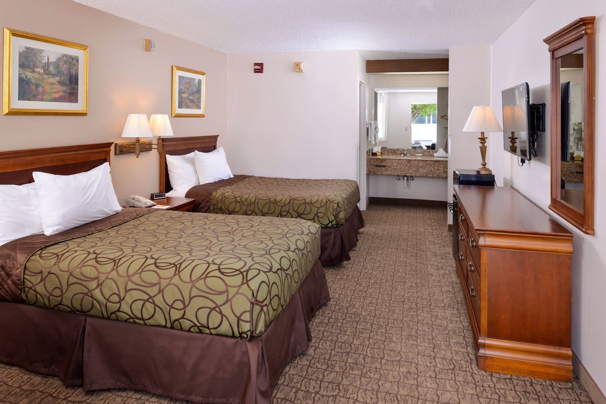 A hotel room with two beds, a dresser, a mirror, and a bathroom visible through an open door.