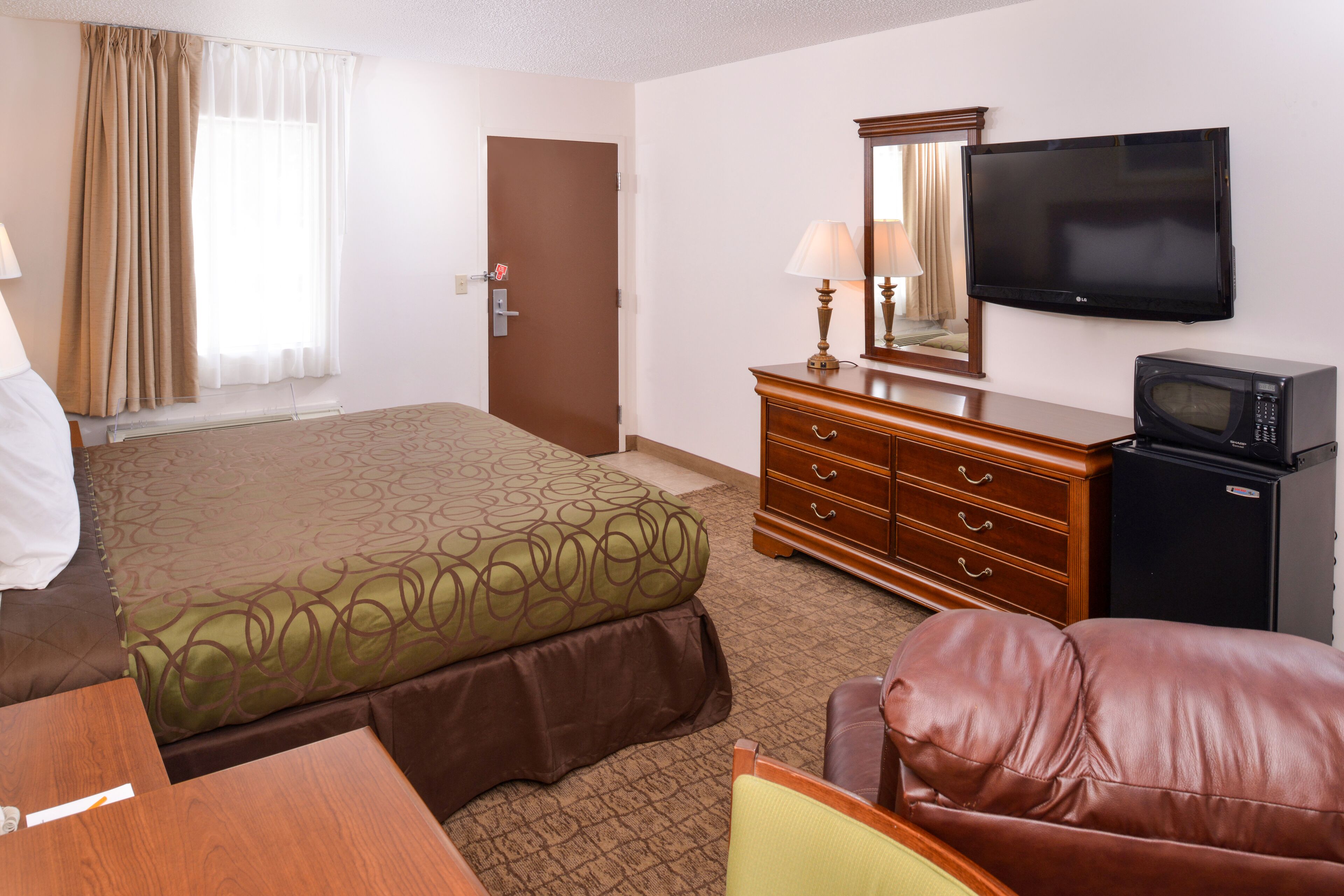 Una habitación de hotel con una cama, un aparador de madera, un televisor, un microondas y un sillón de cuero.