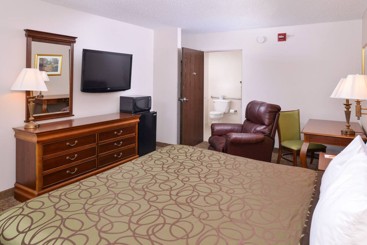 A hotel room with a bed, a dresser, a television, a chair, and a desk.