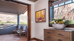 A room with a wooden desk, a chair, a large window with a view of a canyon, and a painting on the wall. - Cable Mountain Lodge (Springdale)