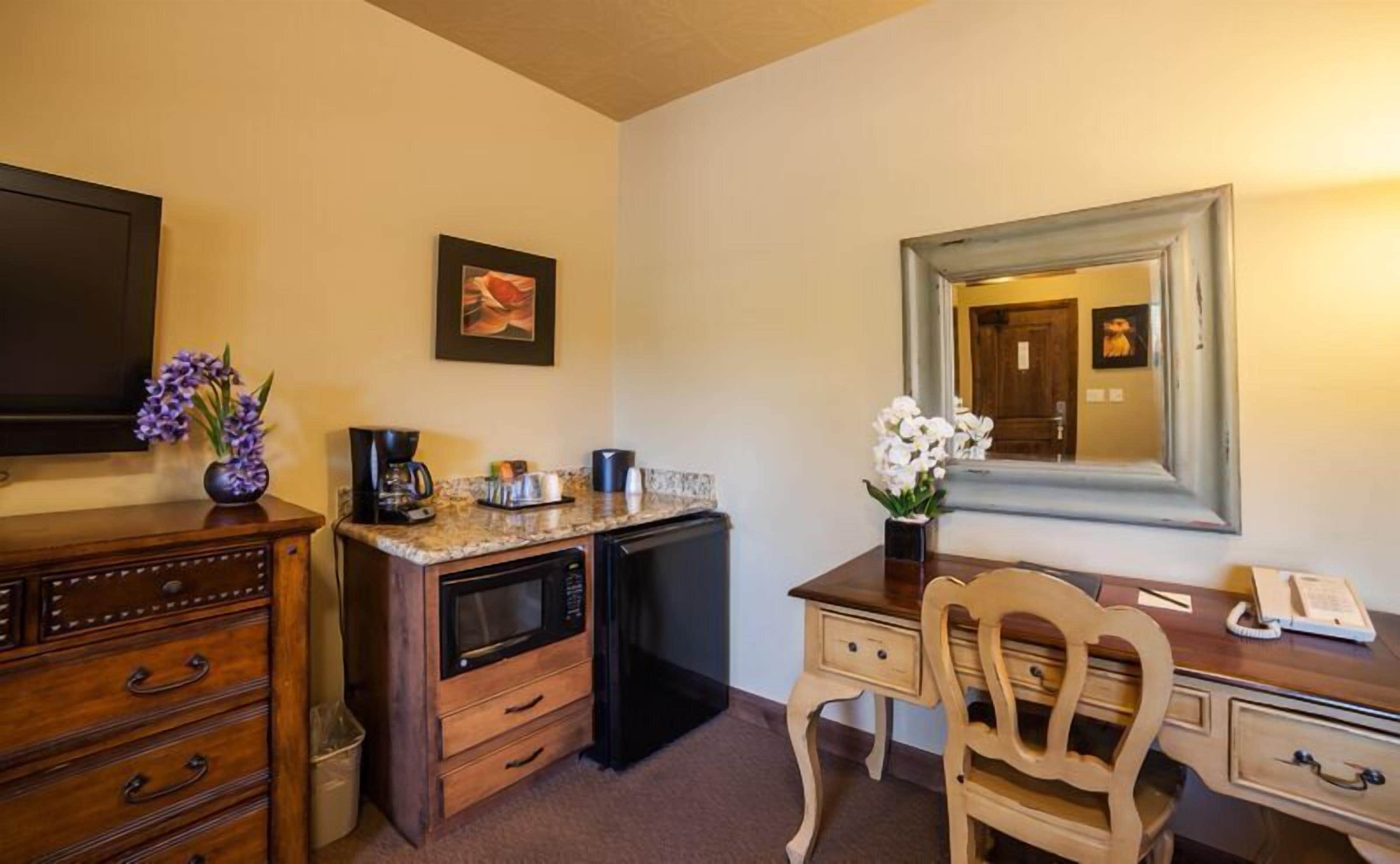 Une chambre d’hôtel équipée d’une kitchenette, d’un bureau en bois, d’une chaise, d’un grand miroir et d’un téléviseur.