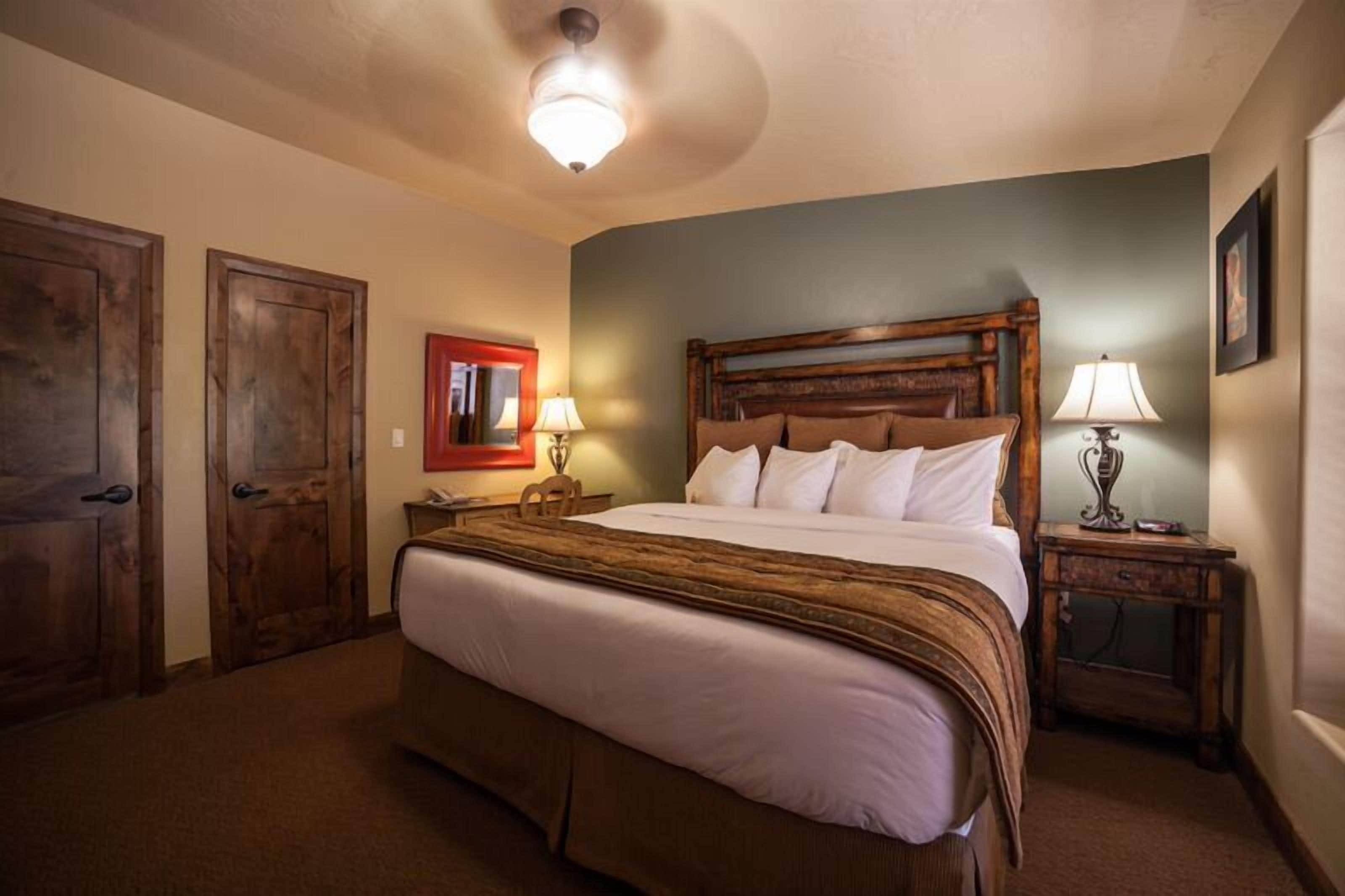 A bedroom with a large bed, two bedside tables with lamps, wooden doors, and a ceiling light fixture.