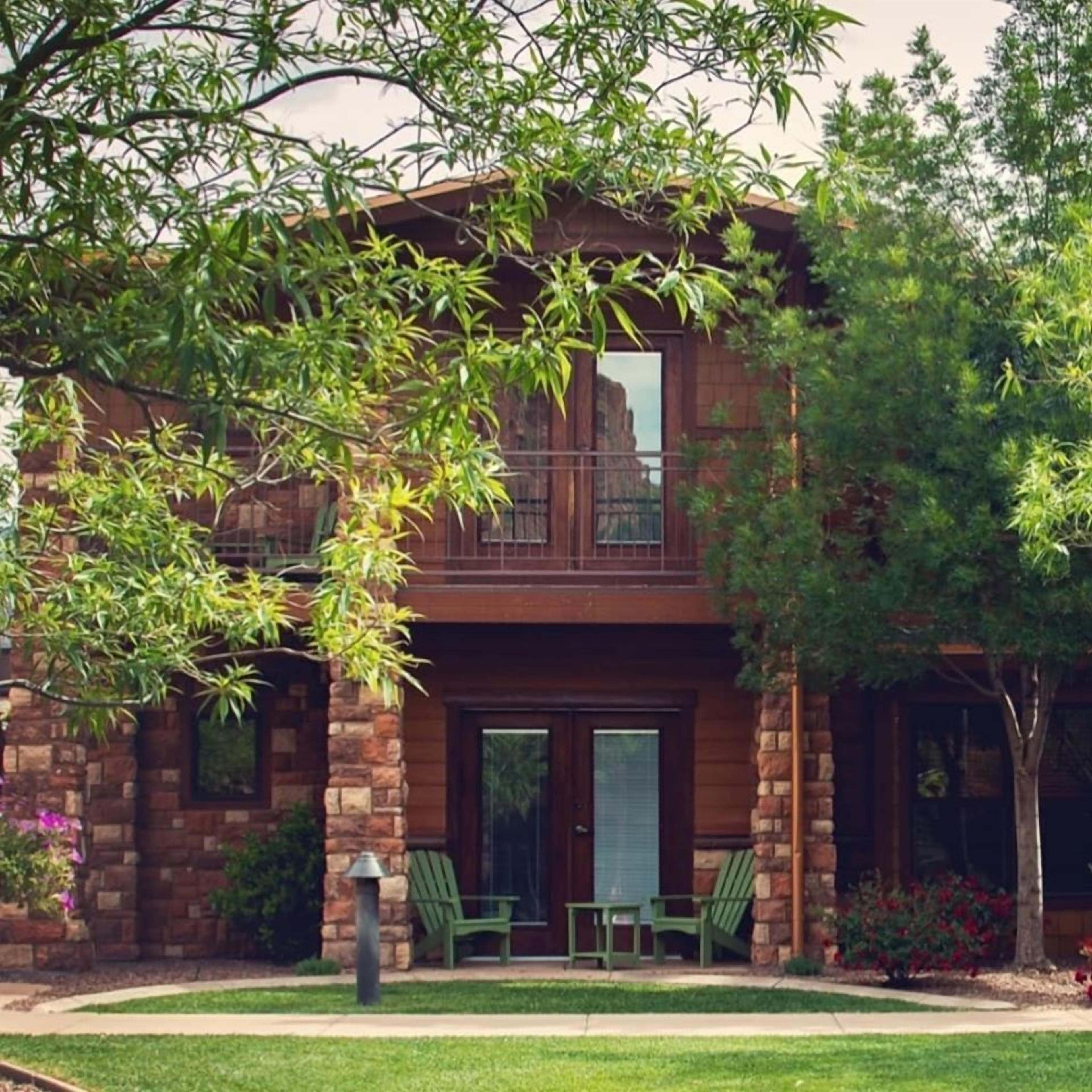 A two-story building with a stone facade, a balcony, and a small front porch with two chairs.