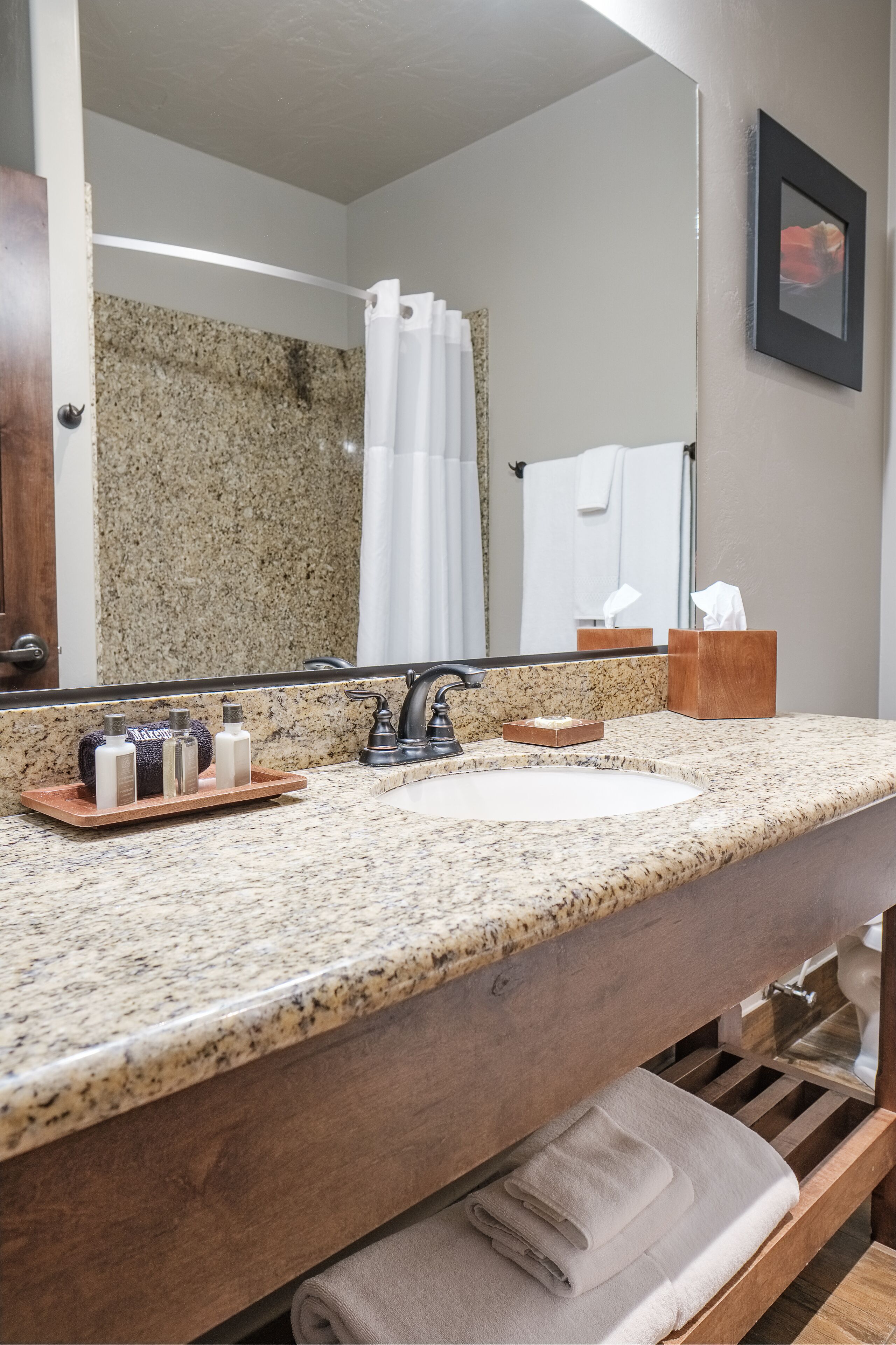 A bathroom with a granite countertop, a sink, a mirror, a towel rack, and a wooden shelf.
