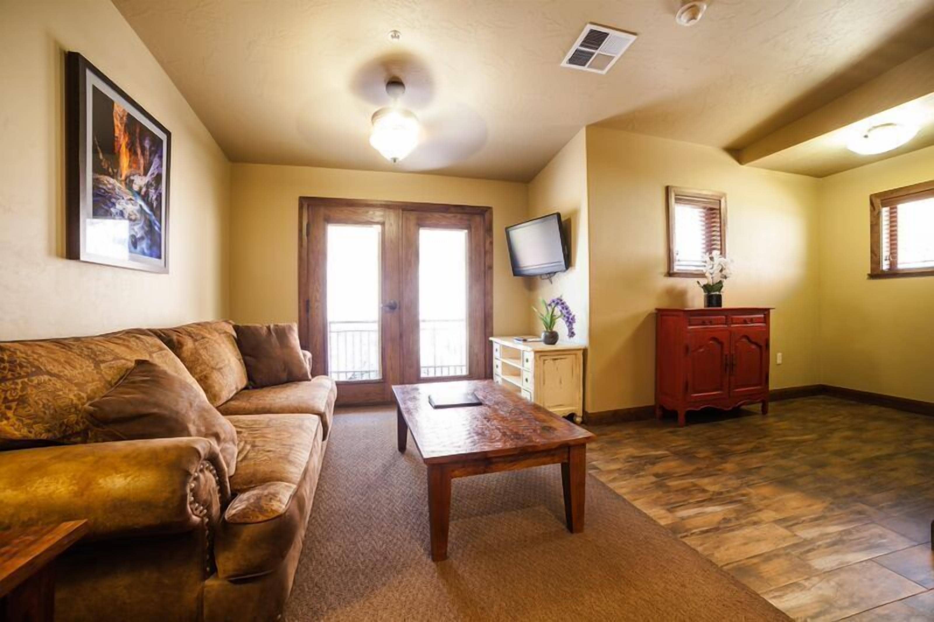 A living room with a brown sofa, a wooden coffee table, a television on the wall, and a cabinet with a plant.