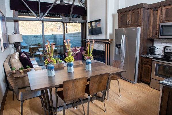 A modern kitchen with wooden cabinets, a stainless steel refrigerator, and a dining area with a wooden table and chairs.