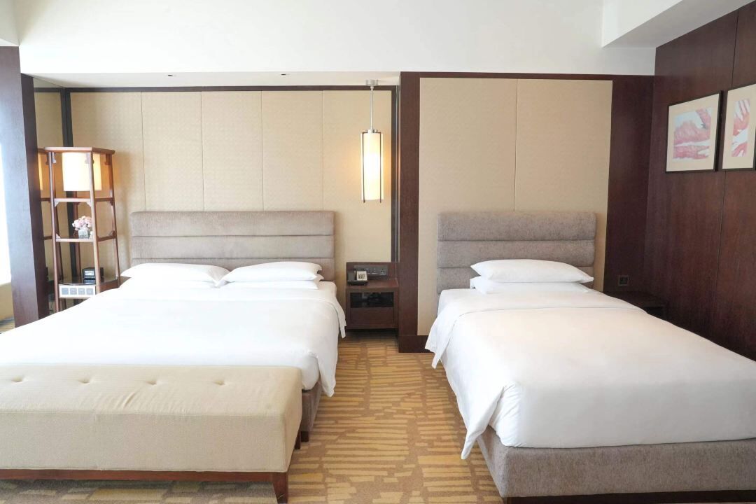 A hotel room with two beds, a nightstand, a lamp, and a bookshelf.