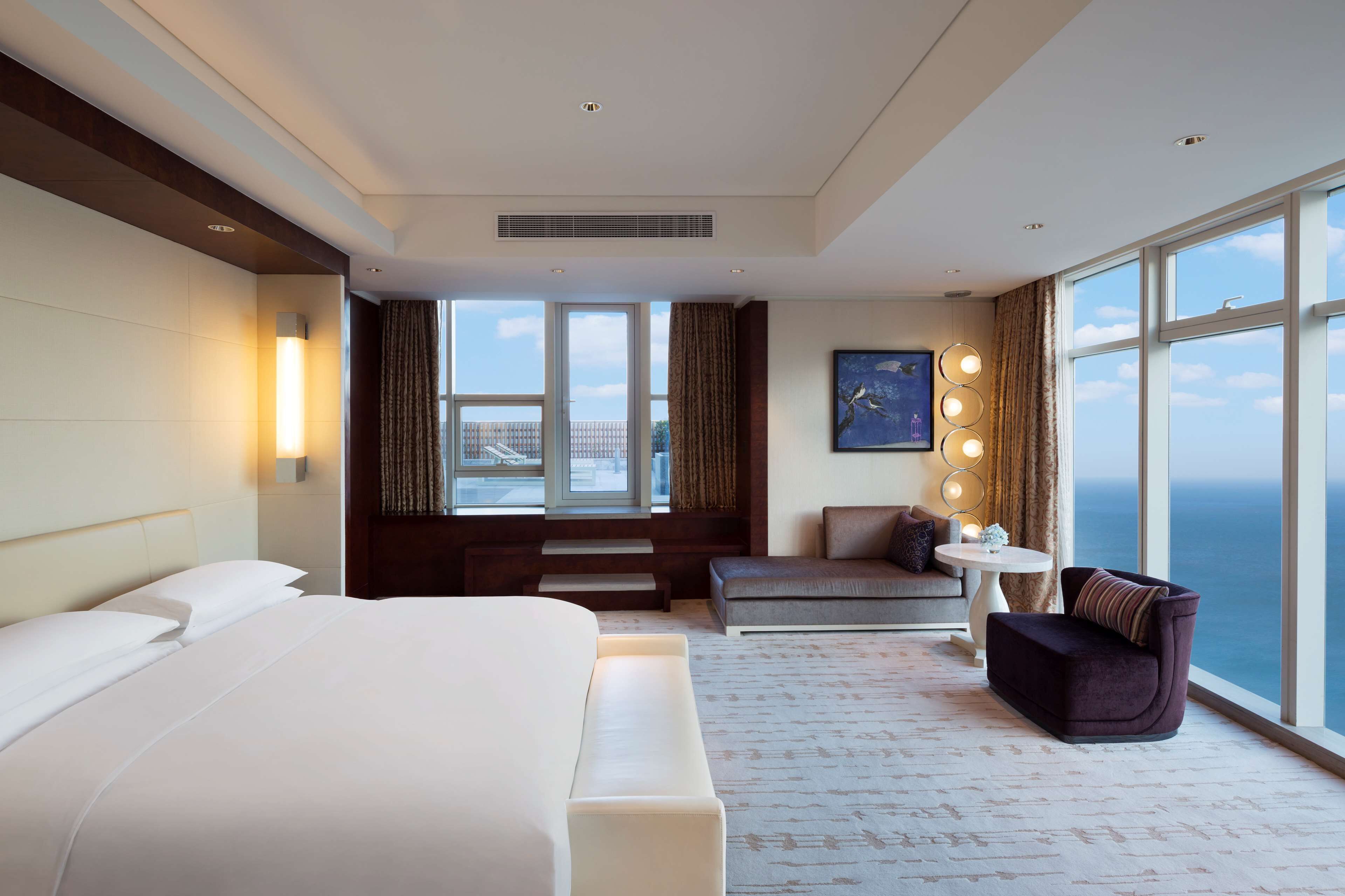 A hotel room with a large bed, a seating area with a view, and a window with curtains.
