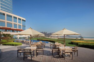 Una terraza en la azotea con mobiliario exterior, piscina y vistas a la playa y las montañas.