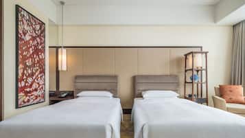 Habitación de hotel con dos camas, un cuadro abstracto de gran tamaño, una mesita de noche con lámpara, un mueble pequeño y una silla con cojín.