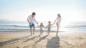 Una familia de cuatro personas caminando sobre una playa arenosa, con el océano al fondo.