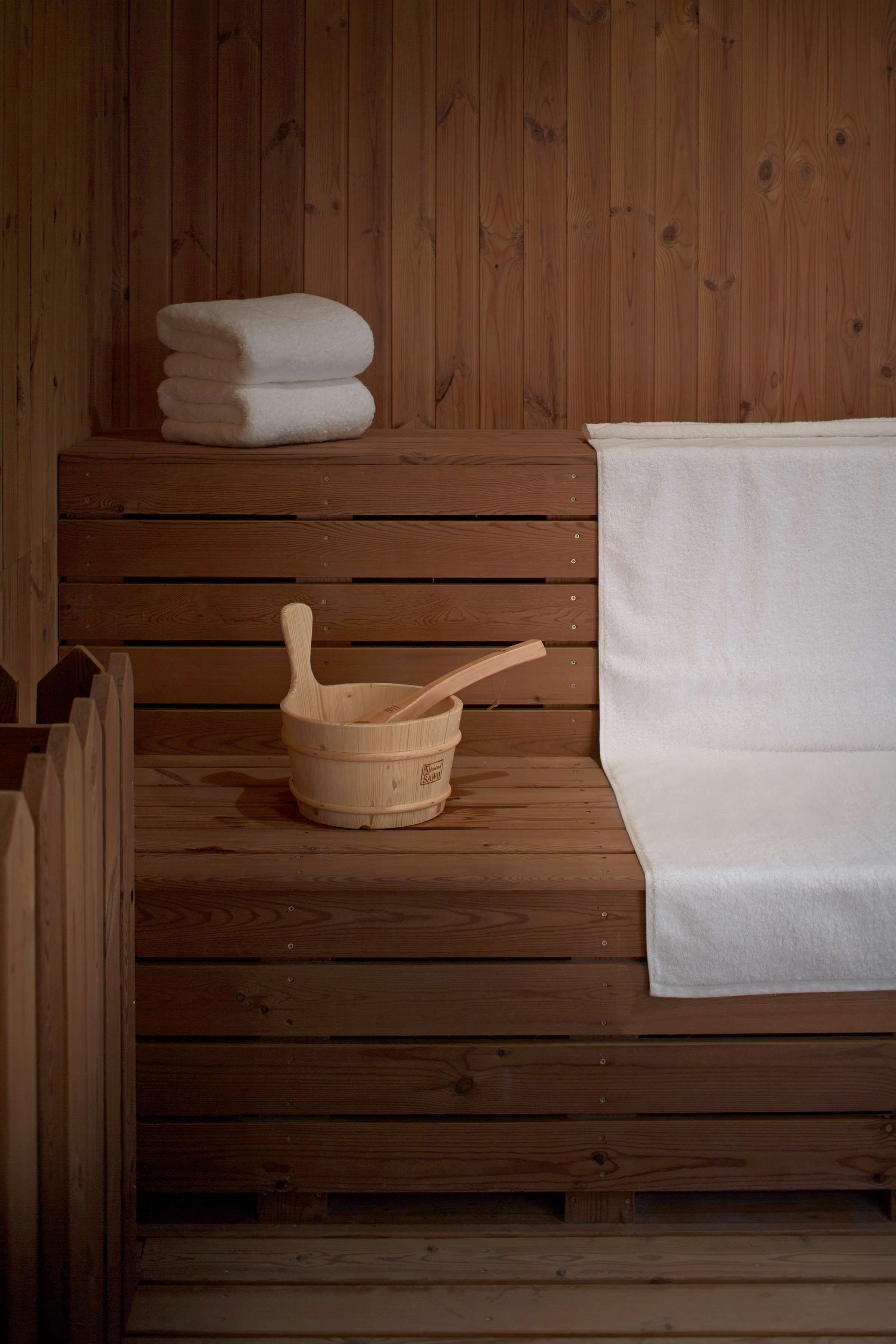 A wooden sauna with a bench, a wooden basin, and stacked towels.
