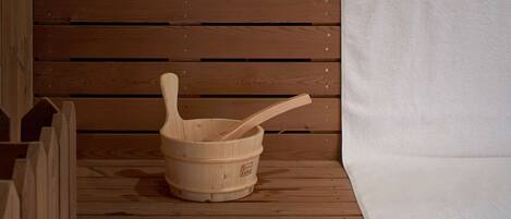 A wooden sauna with a bench, a wooden basin, and stacked towels.