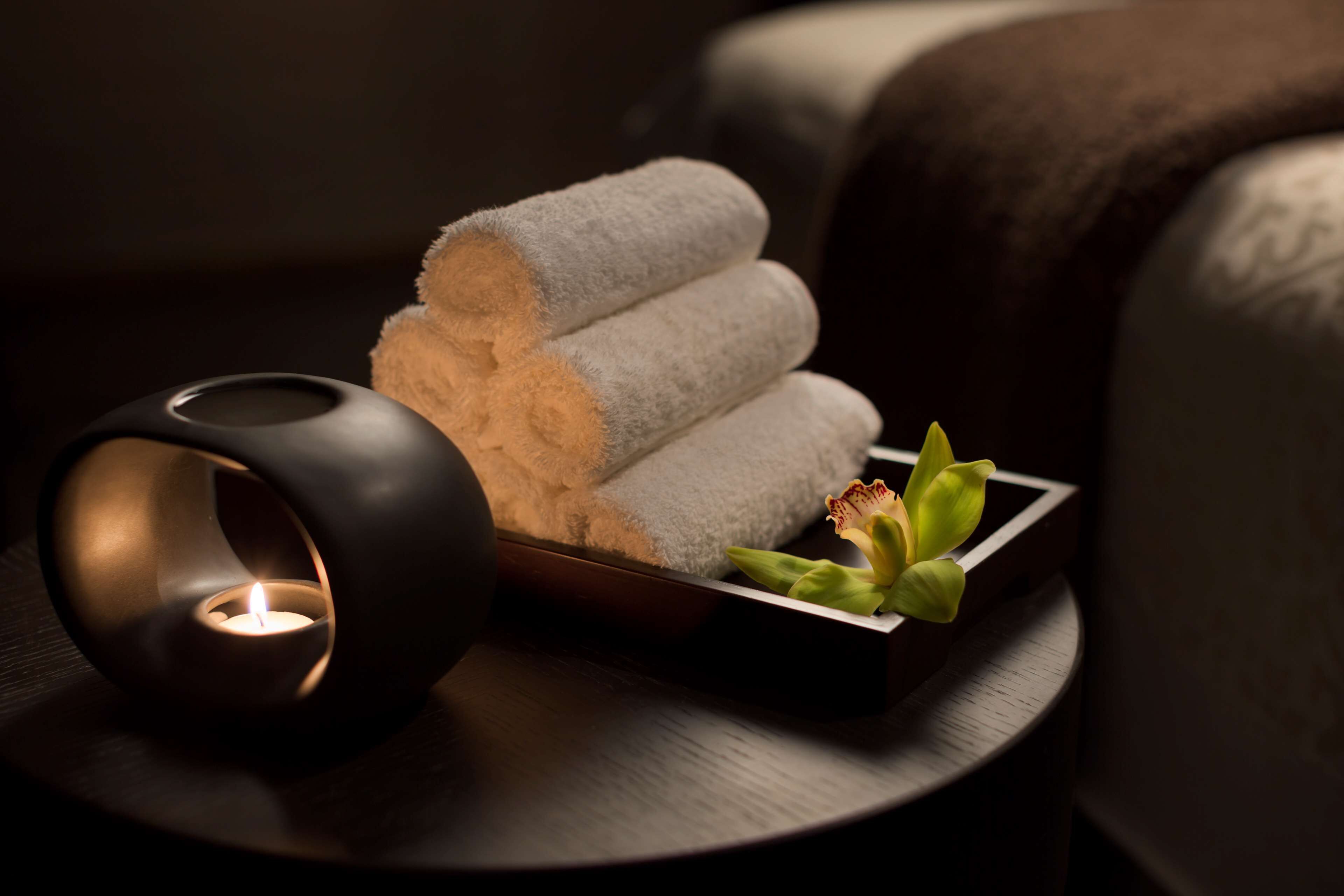 Un ambiente de spa con una vela, toallas enrolladas y un arreglo floral sobre una mesa de madera.