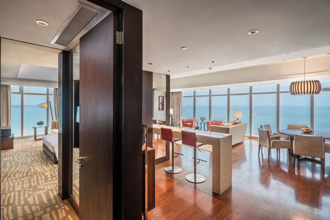 Una habitación de hotel con un ventanal grande, una cama, un escritorio y un comedor.