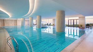 Una amplia piscina cubierta con agua cristalina y azul, rodeada de columnas y sillas de descanso.