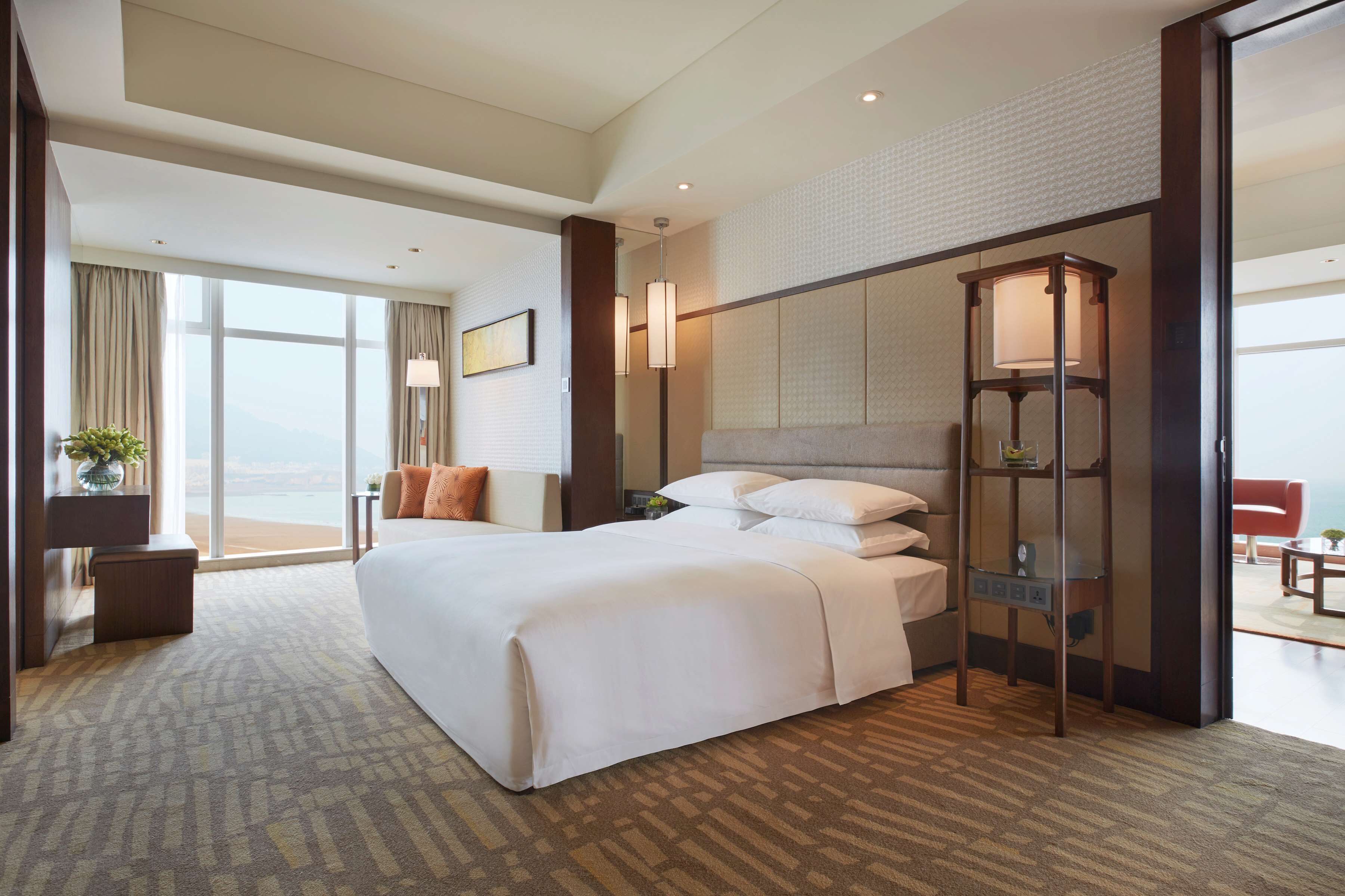 Habitación de hotel con una cama grande, una mesita de noche, una lámpara y vistas al exterior.