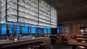 Zona de bar con una gran lámpara de cristal iluminada, mostrador de madera y área de asientos con taburetes de bar.