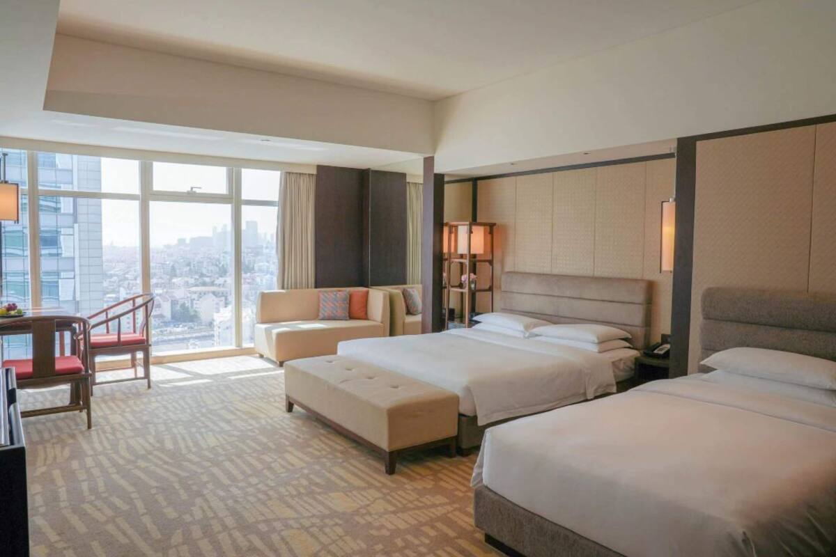 Ett hotellrum med två sängar, en soffa, ett skrivbord och ett stort fönster med utsikt över staden.