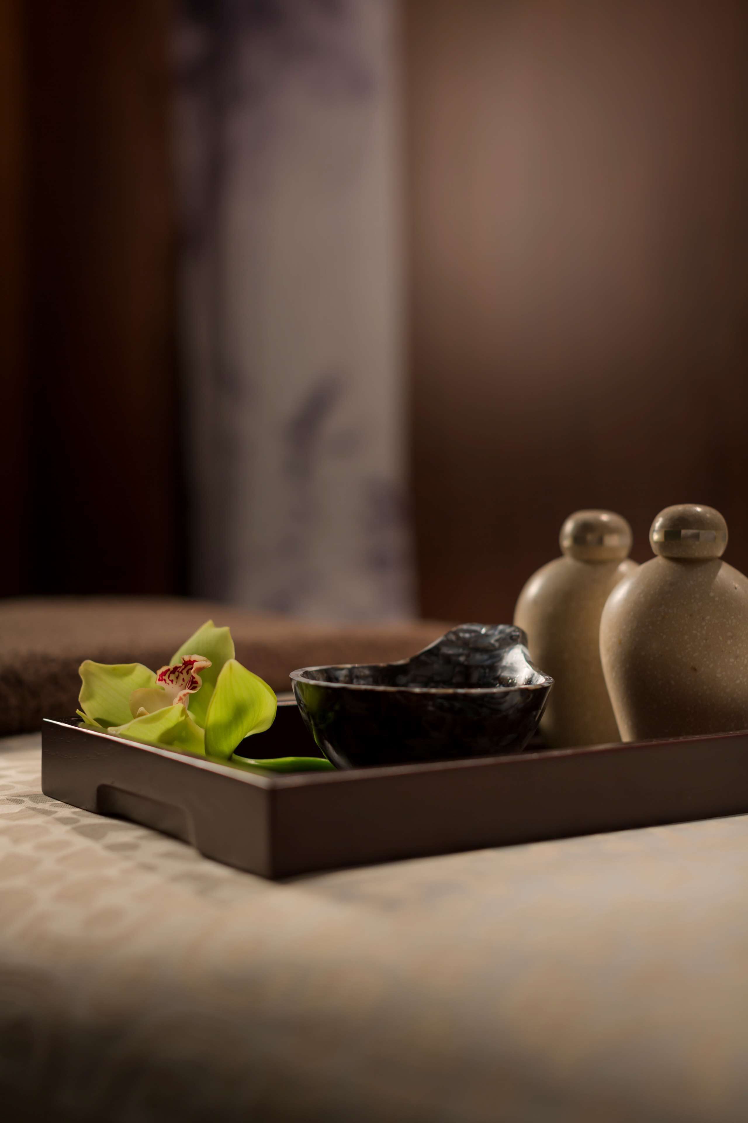 A tray with a green orchid, a black bowl, and two ceramic salt shakers on a textured surface.