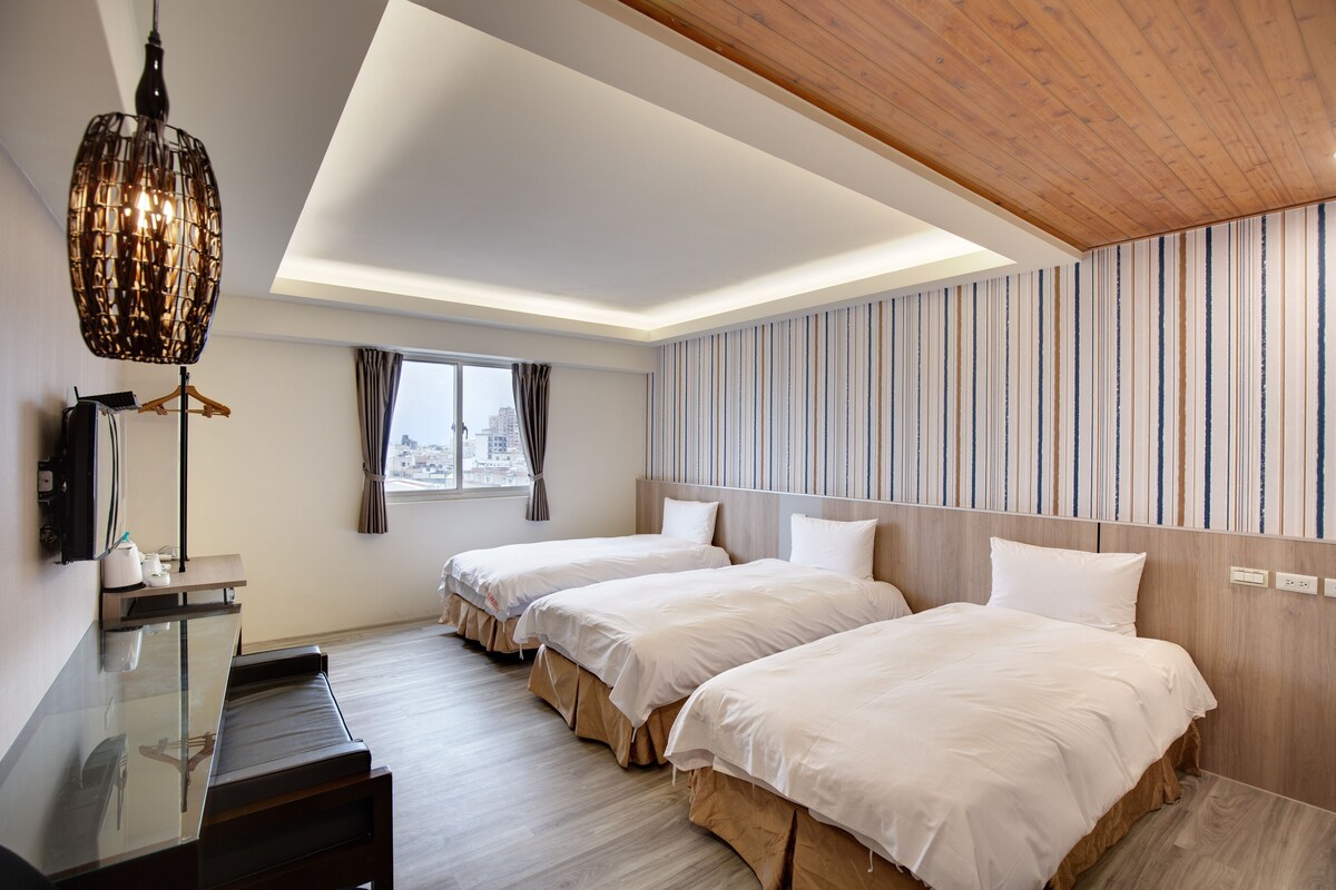 A hotel room with two beds, a wooden ceiling, a striped wall, and a large window.