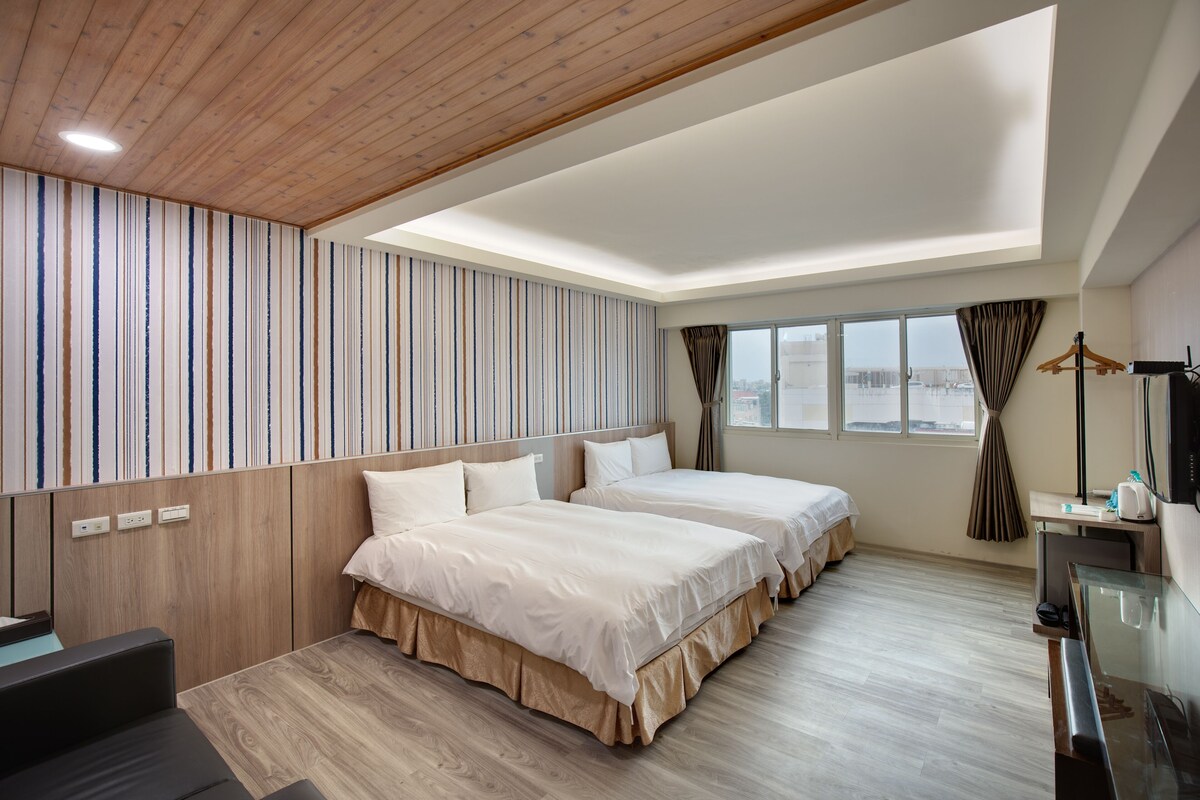 A hotel room with two beds, a desk, a chair, a TV, and a window with curtains.