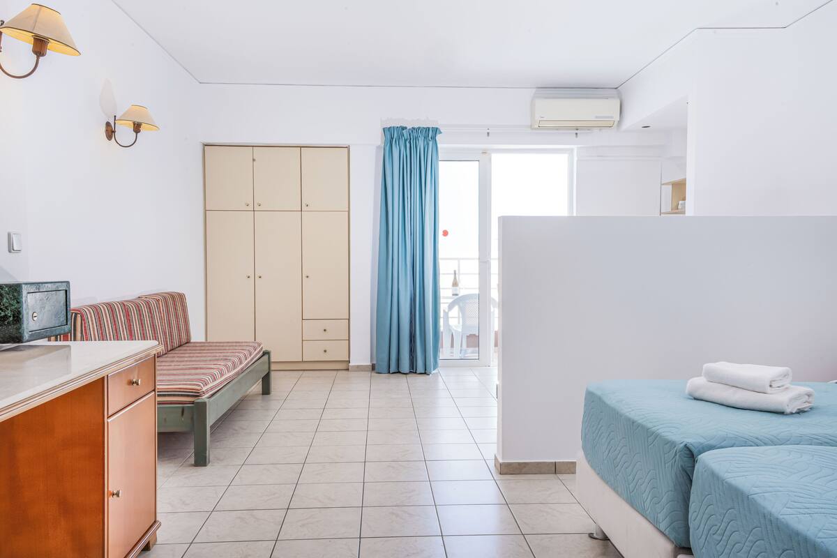 Habitación de hotel con cama, sofá, escritorio, armario y baño visible a través de una puerta.