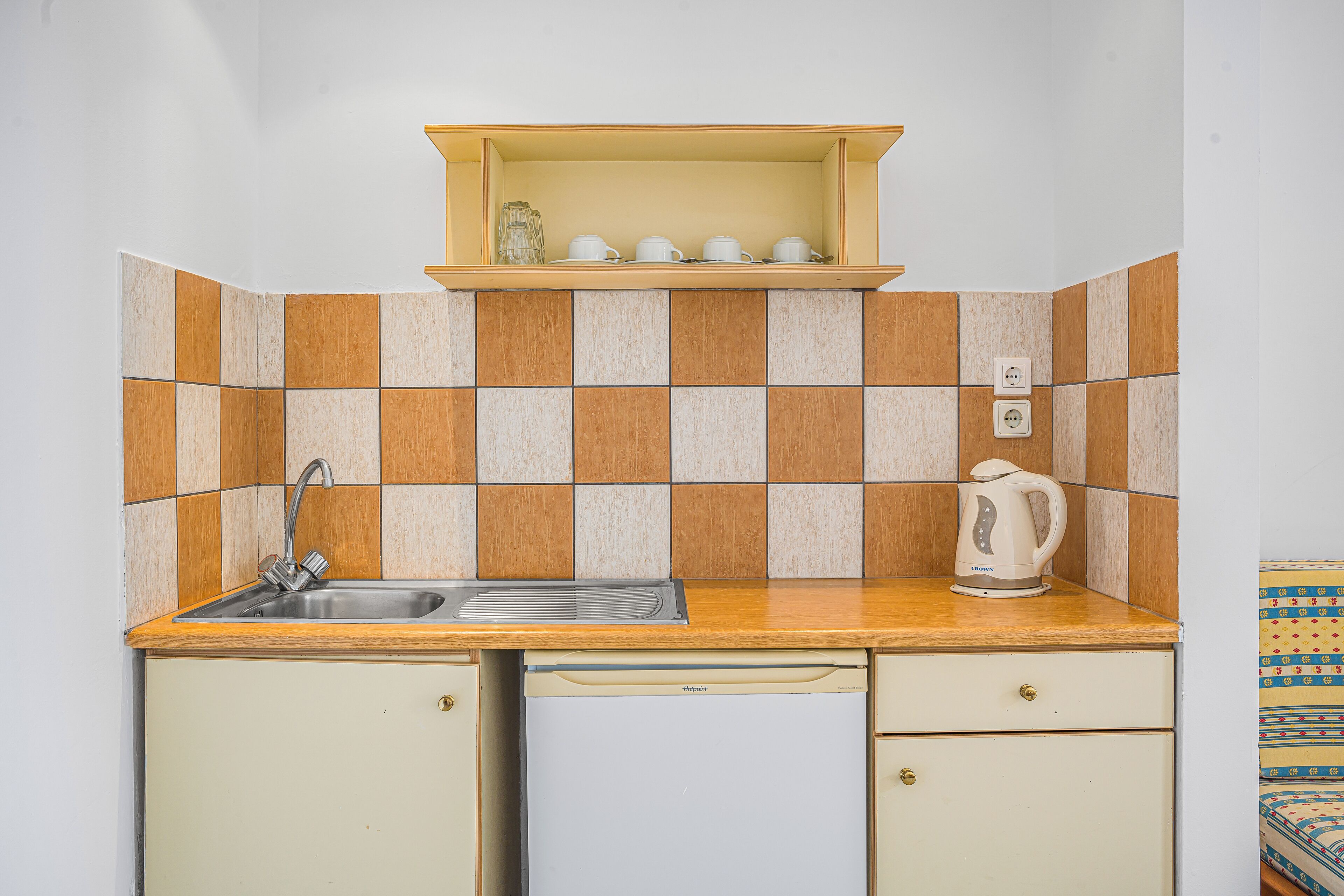 A compact kitchen with a sink, a kettle, and a shelf above the counter.