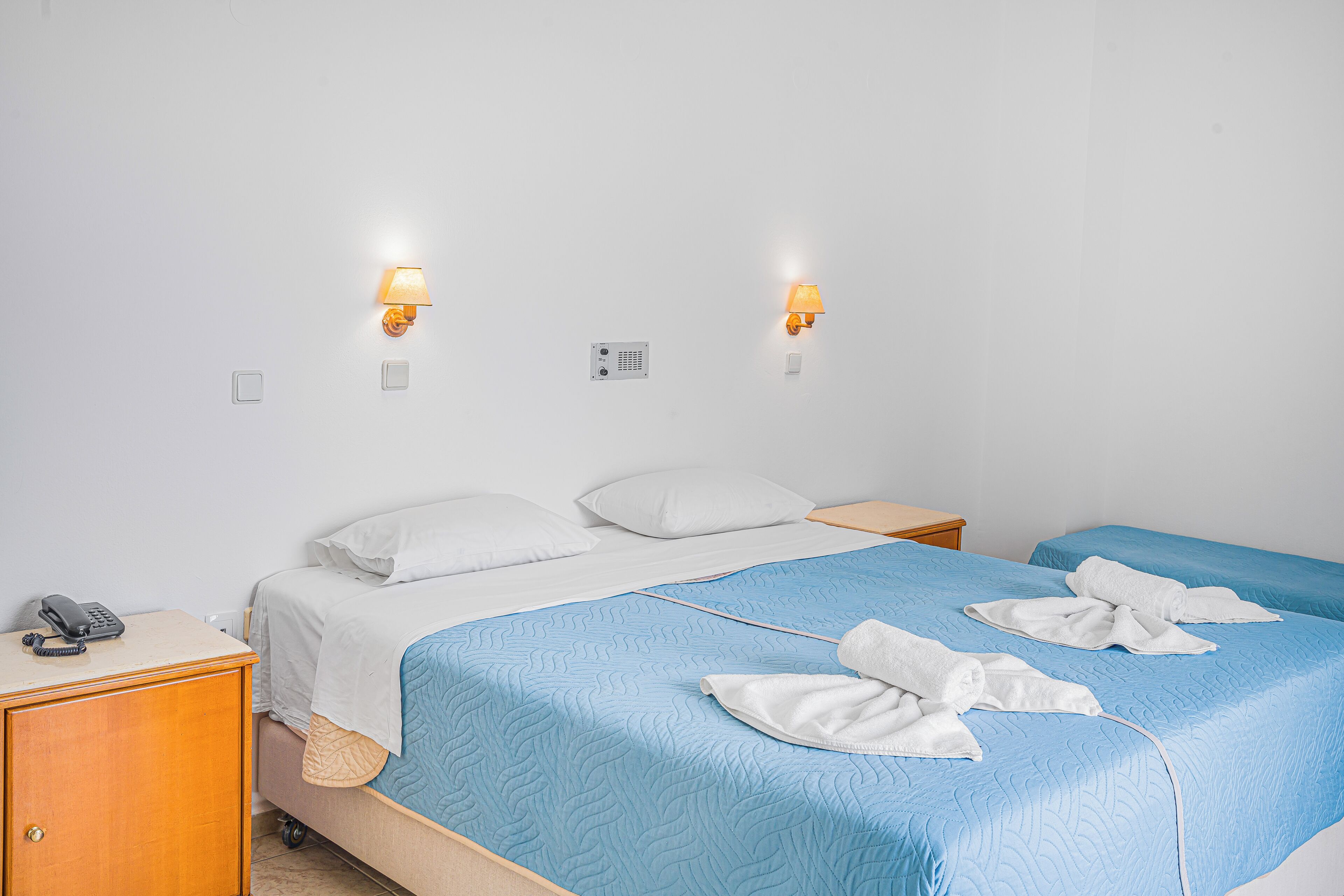 A hotel room with a bed, two bedside tables, a phone, and two wall-mounted lamps.