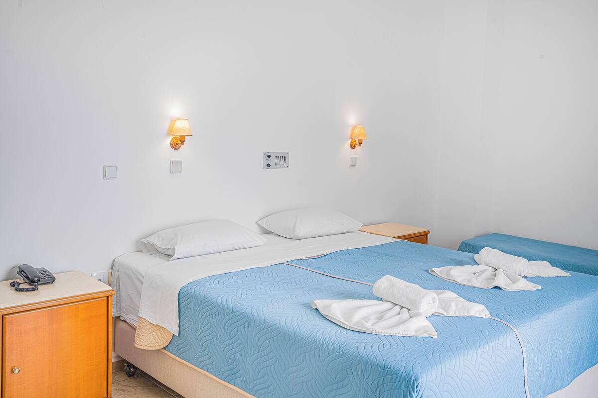 Una habitación de hotel con una cama, dos mesitas de noche, un teléfono y dos lámparas de pared.