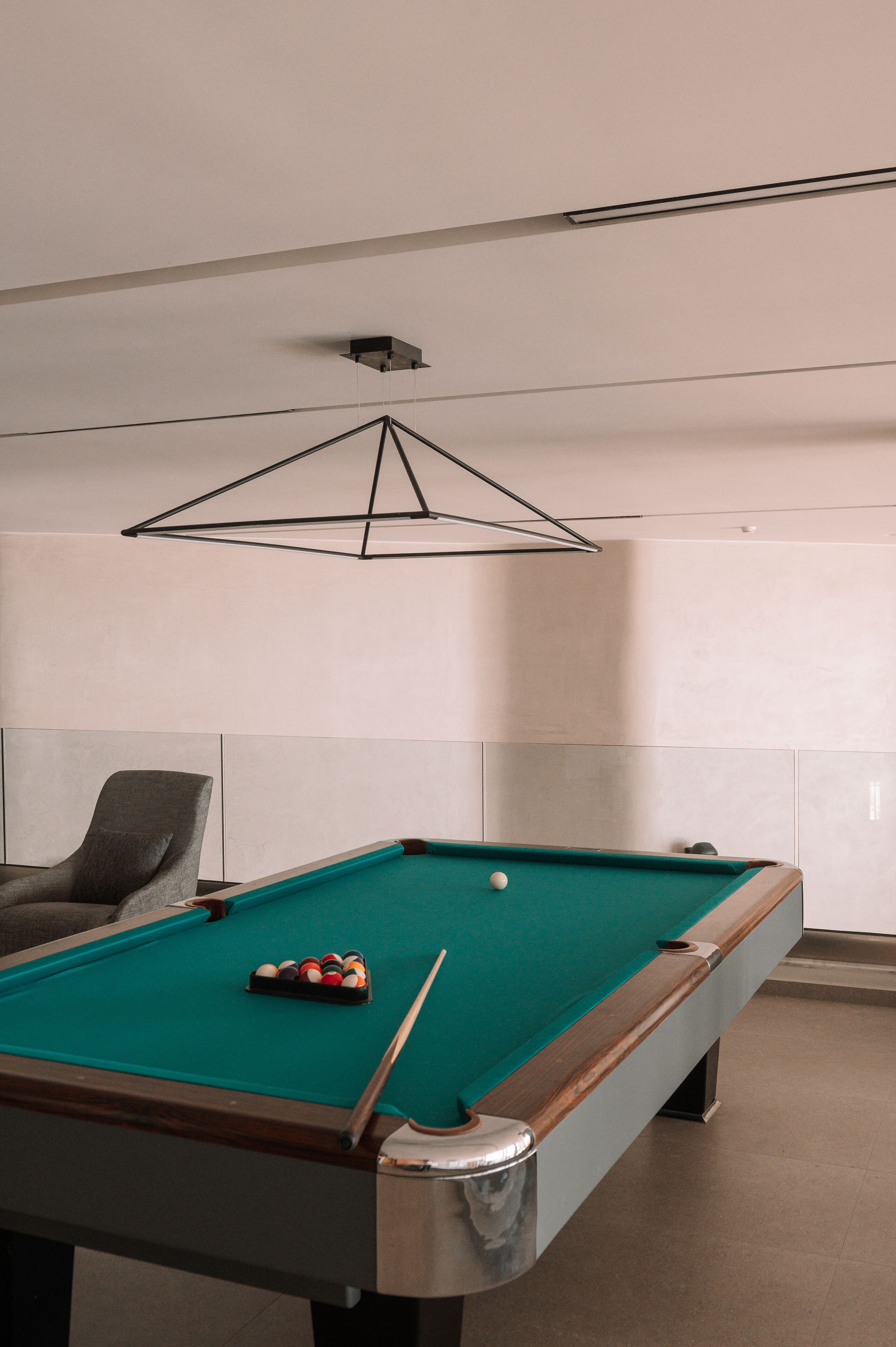 A pool table with balls, a cue stick, and a modern geometric light fixture.
