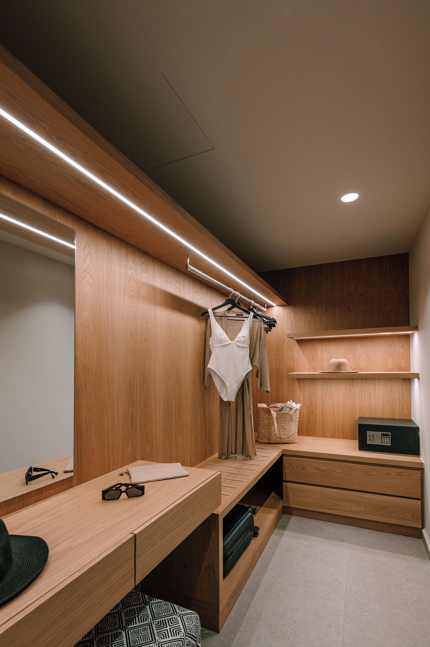 A modern, well-lit walk-in closet with wooden cabinetry, a hanging rack, and a desk area with a basket and a small electronic device.