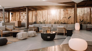 A modern lounge area with seating arrangements, a central fire feature, and a decorative wall with vertical elements. - Unique Blue! Resort and Villas Adults Only (Hersonissos)