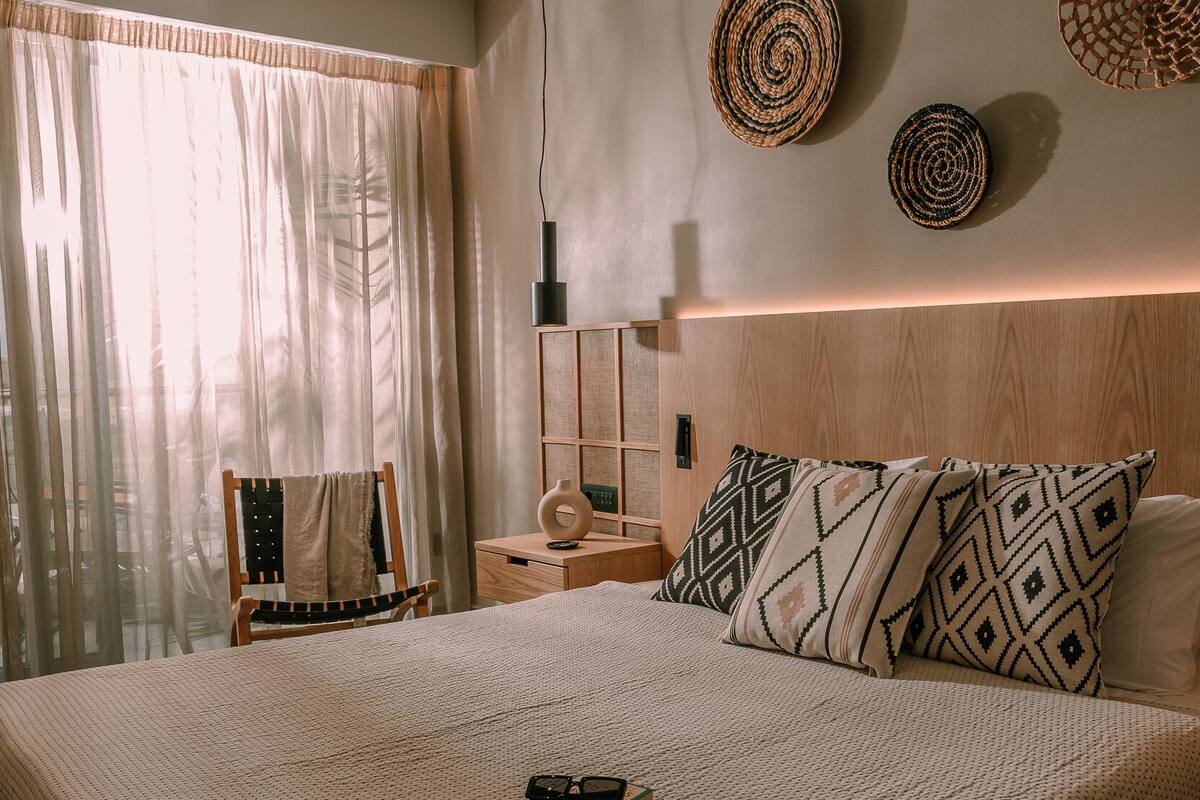 Ein Schlafzimmer mit einem großen Bett, einem Deckenventilator, einem Nachttisch mit Lampe und Blick auf einen Balkon mit Vorhängen.