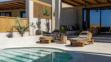 A modern outdoor pool area with lounge chairs, a wooden deck, and a covered seating area.