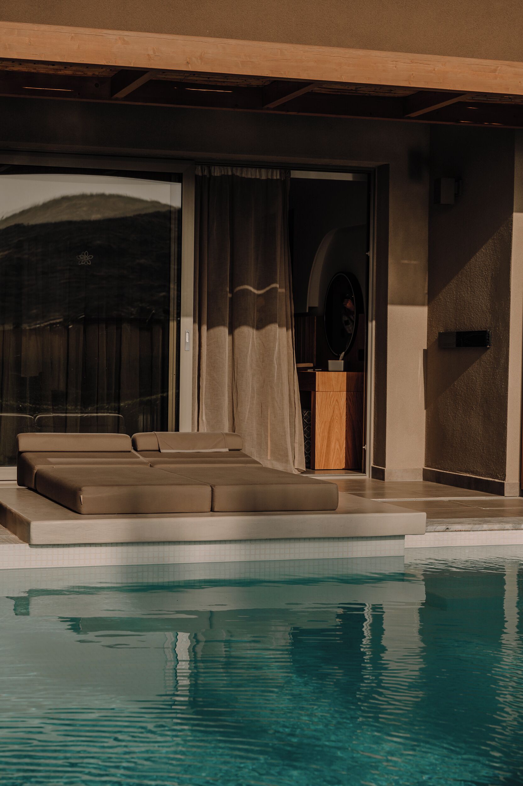 A modern pool area with a clear view of the pool, a seating area with cushions, and a wooden cabinet.
